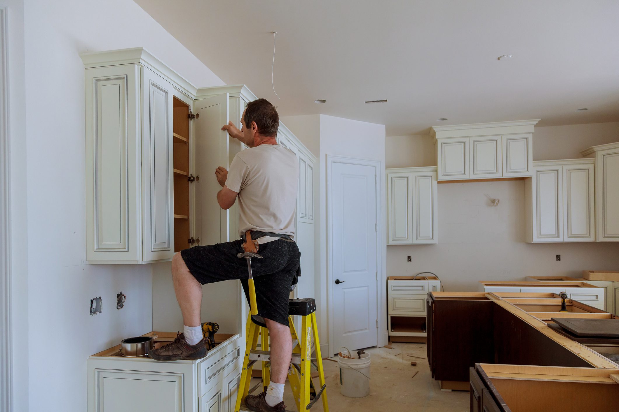 Man installing kitchen cabinets on ladder.