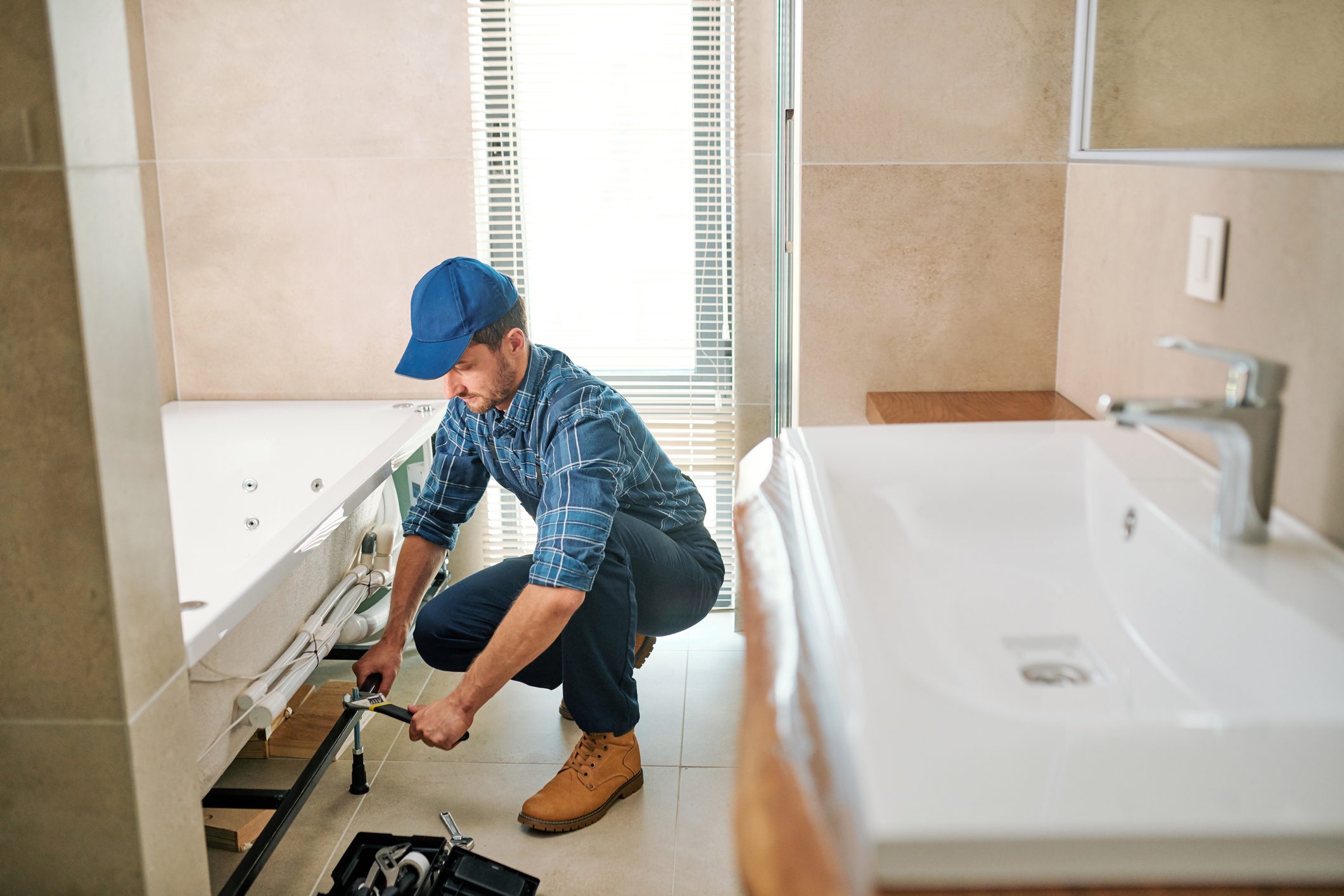 Plumber fixing bathroom pipes with tools.